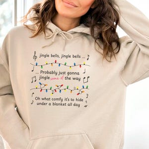 May include: A beige hoodie with a musical note design and the text "jingle bells, jingle bells... Probably just gonna jingle some of the way. Oh what comfy it's to hide under a blanket all day."