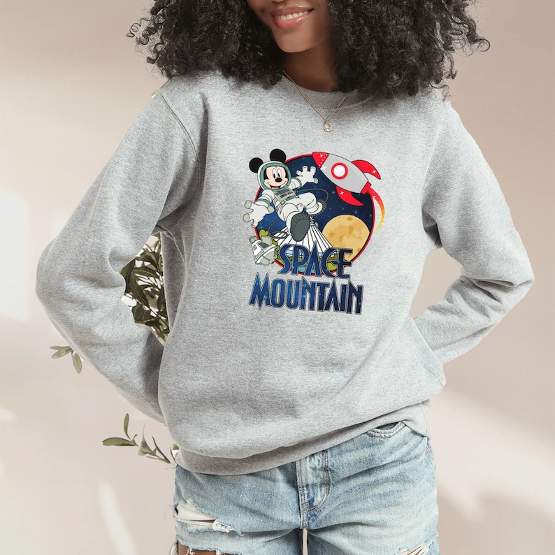 Op de afbeelding: Een grijs sweatshirt met een afbeelding van Mickey Mouse als astronaut in de ruimte. De afbeelding bevat een raket, een planeet en de tekst "Space Mountain".