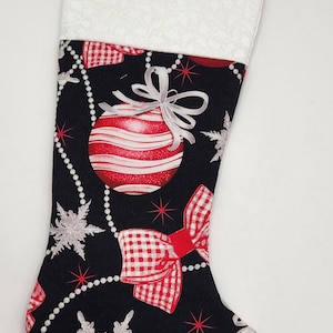 May include: A Christmas stocking featuring a black fabric base with a pattern of red and white striped ornaments, red and white gingham bows, silver snowflakes, and draped beaded garlands. The top cuff is white with a subtle tonal pattern.
