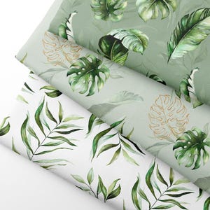May include: Three rolls of fabric with watercolour botanical designs. The fabrics feature green leaves and gold accents on a white and green background. The designs include tropical leaves and ferns.