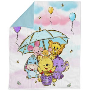 May include: A baby blanket with a colourful illustration of Winnie the Pooh and friends. The design includes a light blue umbrella, balloons, bees, and the word "Hunny" on a purple pot. The blanket has a light blue backing.