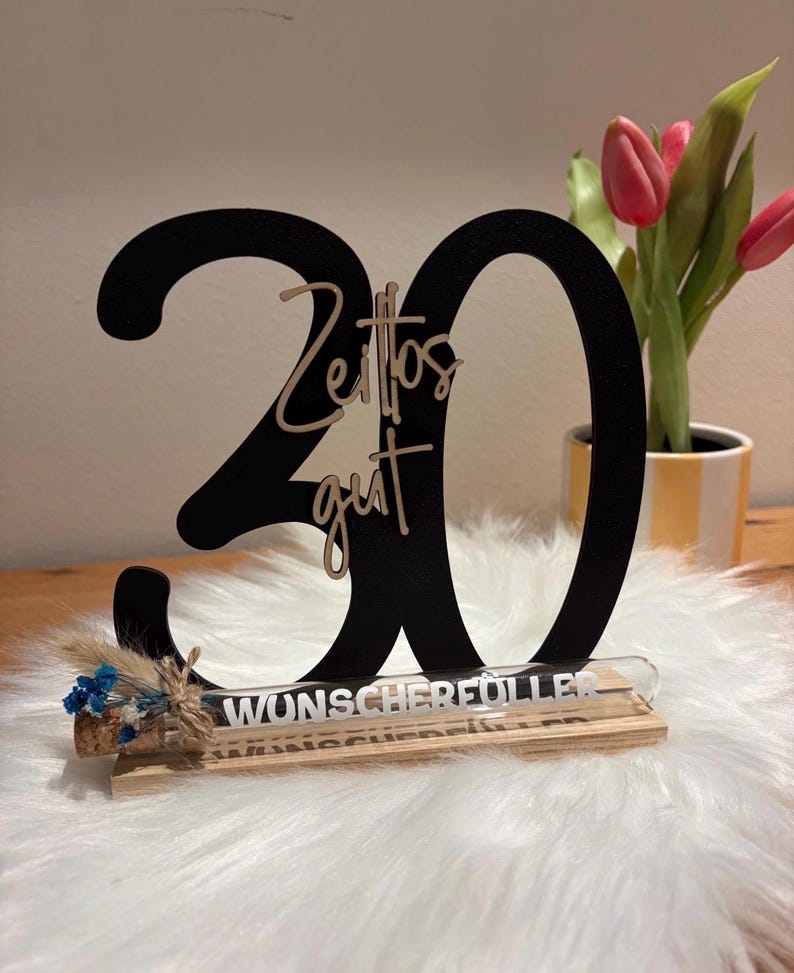 May include: A black wooden '30' birthday decoration with the words "Zeitos gut" in a lighter color. A small glass tube with text is attached to a wooden base, decorated with dried flowers.