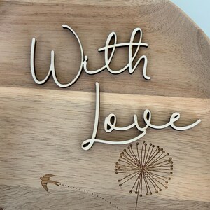 May include: Wooden decorative tray with the words "With Love" in a cursive font. The tray features a laser-etched dandelion design and a flying bird. The tray is made of light-colored wood.