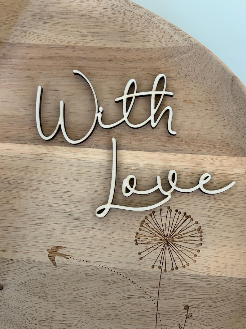 May include: Wooden decorative tray with the words "With Love" in a cursive font. The tray features a laser-etched dandelion design and a flying bird. The tray is made of light-colored wood.