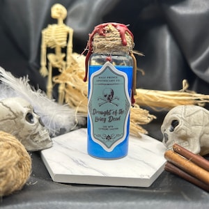 May include: A small blue glass bottle with a cork stopper and a red wax seal. The bottle is labeled "Drought of the Living Dead" with a skull and crossbones graphic. The label also reads "Half Prince Apothecary Co."