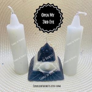 May include: Three white candles with the text "CANDLE OF SECRETS" printed on them, and a black pyramid candle with a white eye and the text "CANDLE OF SECRETS" printed on it. The pyramid candle is in the centre of the image, and the white candles are on either side. The text "OPEN MY 3RD EYE" is printed on a black circle above the candles.