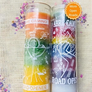 May include: Two glass jar candles with colorful wax layers and white text. The candles are labeled "Abre Camino" and "Road Opener". The text on the candles includes the words "Health", "Business", "Love", "Money", and "Success".