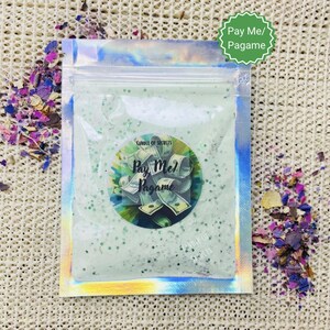 May include: A clear green glitter candle in a silver pouch with the text "Candle of Secrets" and "Pay Me/Pagame" on the label.