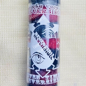 May include: A black and red candle with the text "Siete Veces Reversible" and "Seven Times Reversible" printed on it. The candle is in a glass jar and has a white wick.