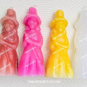 Op de afbeelding: Vier staande waskaarsen in de vorm van mensen met hoeden. De kaarsen zijn in de kleuren roze, oranje, geel en wit.