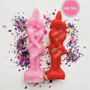 May include: Two pink and red love spell candles with the text "Candle of Secrets" on each. The candles are shaped like a couple embracing. The candles are surrounded by pink and purple confetti. The text "Love Spell" is written on a pink circle.