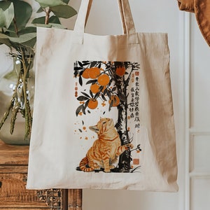May include: A beige tote bag with a design of a cat sitting under a tree with oranges. The text on the bag reads "有楽町", "吉兆", "招福", "寿", "福", "春", "招財進寶", "財源廣進", "萬事如意", "心想事成", "恭喜發財", "新年快樂".