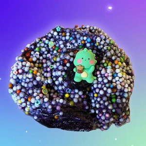 May include: Purple slime with colorful beads and a green cartoon character holding a cup. The slime is in a galaxy-themed background.