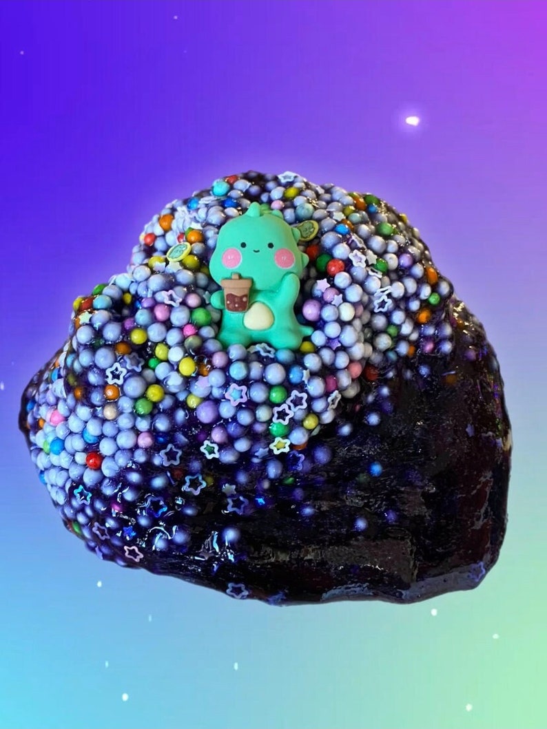 May include: A purple slime with a green cartoon character holding a cup of boba tea. The slime is covered in colorful sprinkles and stars.
