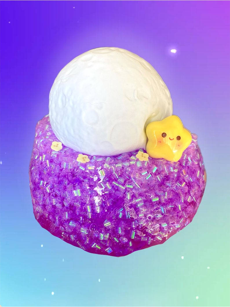 May include: A whimsical, handcrafted slime creation featuring a large, white, textured moon on top of a sparkling purple base. A yellow star with a smiling face is attached to the side, with small yellow flower accents.