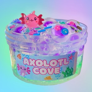 May include: A clear plastic container filled with purple and clear slime, decorated with colorful sprinkles, small charms, and a pink axolotl figure. The container has a label that reads "AXOLOTL COVE" with axolotl and aquatic illustrations.