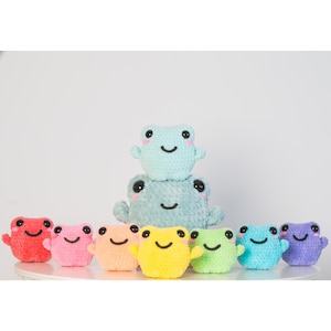 May include: A set of nine plush frog toys in various colors, including red, pink, orange, yellow, green, blue, and purple. The frogs are arranged in a row, with the largest frog in the center and the smaller frogs on either side. The frogs have smiling faces and large eyes.