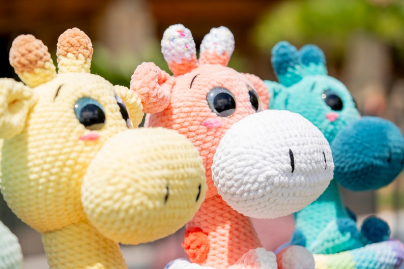 May include: Three crocheted giraffe toys, one yellow, one pink, and one blue, with large eyes and a textured surface.