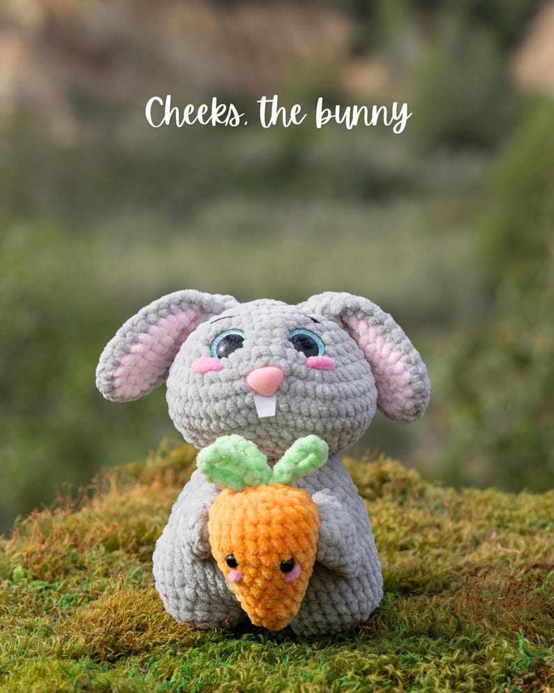 Puede incluir: Un conejito de crochet gris sosteniendo una zanahoria de crochet naranja. El conejito tiene mejillas rosadas y ojos azules. El texto "Cheeks. the bunny" est&aacute; por encima del conejito.