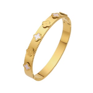 May include: A gold bangle bracelet with a textured surface and white flower accents.