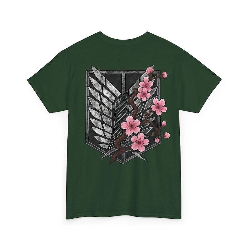 May include: Dark green t-shirt featuring a graphic design. The design includes a stylized emblem with wings and a branch of pink cherry blossoms. The shirt is made of a soft material.