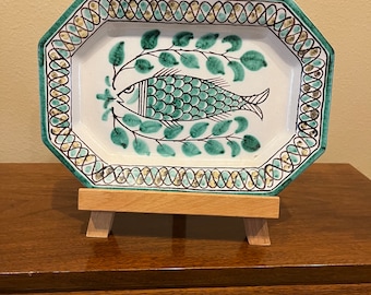 May include: A white ceramic serving dish with a green and gold border. The dish features a green fish with black details and green leaves on a white background.