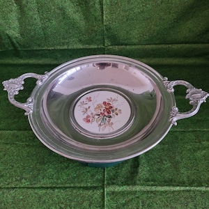 May include: A silver serving dish with two handles and a white porcelain insert with a floral design. The floral design features pink, red, and green flowers.