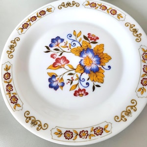 Puede incluir: Plato de cerámica blanco con borde dorado y un diseño floral en tonos azules, rojos y amarillos.