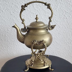 May include: A vintage brass teapot with an ornate design and a stand. The teapot has a lid and a spout, and the stand has three legs.