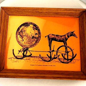 May include: A framed image of a bronze chariot with a goat pulling it. The image is on a copper background and has the text "Solegnas Fra Trondhjem-Broncealder CA. 1000 F.KR." at the bottom.