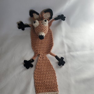 May include: A handmade crochet fox with a tan body, black paws, and a white and tan tail. The fox has large, googly eyes and is posed with its arms outstretched. The fox is a whimsical, handcrafted item.