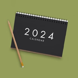 May include: A black spiral bound calendar with the year 2024 printed in white on the front cover. The text "CALENDAR" is printed below the year.