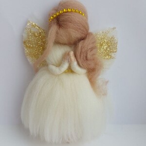 Pode incluir: Um pequeno anjo de feltro branco com asas de glitter dourado e uma auréola de feltro marrom. O anjo está com as mãos juntas em posição de oração.