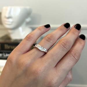 Peut inclure: Une bague en argent avec un design texturé et organique. La bague est sur le doigt d'une personne.