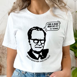 May include: White t-shirt with a black and white graphic of B.F. Skinner, the quote "CAN A DEAD MAN DO IT?" and the text "WORLD BEHAVIOR ANALYSIS DAY!". The shirt is made of a soft, comfortable material.