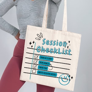 Puede incluir: Bolso tote color crema con las palabras "Session Checklist" en azul. La lista de verificación incluye "Pair w/Client", "Run Goals", "Have Fun" y "Write Session Notes". La bolsa tiene líneas negras y casillas de verificación.