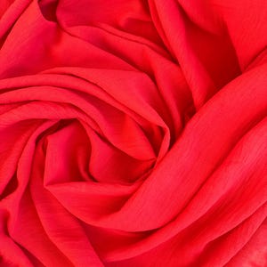 Pode incluir: Tecido vermelho vibrante com superfície texturizada, habilmente drapeado e dobrado. As dobras criam sombras e realces, realçando a cor vibrante. O material parece leve e fluido, adequado para vestuário ou projetos decorativos.