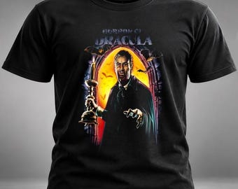 Könnte beinhalten: Ein schwarzes Kurzarm-T-Shirt mit einem Grafikdruck des Filmplakats Horror of Dracula. Das Motiv zeigt einen Vampir, der eine brennende Kerze in einem steinernen Torbogen hält, während Fledermäuse vor einem hellgelben Hintergrund fliegen.