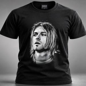Könnte beinhalten: Ein schwarzes Kurzarm-T-Shirt mit einem großen, zentrierten, einfarbigen Fotodruck einer Person mit schulterlangem Haar. Das T-Shirt hat einen Rundhalsausschnitt und ein Gildan-Markenetikett, das im inneren Kragenbereich sichtbar ist.