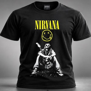 May include: A black short-sleeved t-shirt featuring the yellow text NIRVANA above a yellow smiley face graphic. Below the smiley face is a black and white photographic print of a person sitting while holding an electric guitar.
