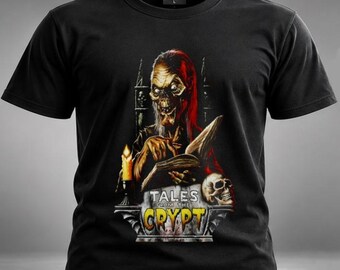 Könnte beinhalten: Ein schwarzes Kurzarm-T-Shirt mit einem Grafikdruck einer skelettartigen Figur, die bei Kerzenschein in einem Buch liest. Das Design zeigt einen Totenkopf und den Schriftzug "TALES FROM THE CRYPT" in gelben und weißen Buchstaben.