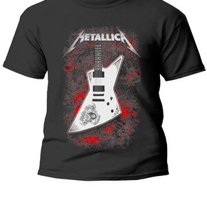 Puede incluir: Camiseta negra con un gráfico de guitarra eléctrica blanca y el nombre de la banda "Metallica" en plata. El diseño de la guitarra incluye un efecto de salpicaduras rojas. Prenda de vestir con temática musical.