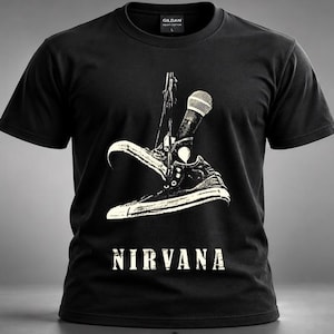 May include: A black short-sleeved crew neck t-shirt featuring a white graphic print of a trainer hanging from a microphone. The word NIRVANA is printed in white capital letters below the graphic. The shirt has a Gildan brand label at the neck.