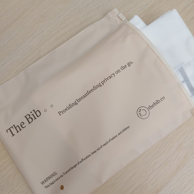 May include: A beige zippered pouch with the text "The Bib" and "Providing breastfeeding privacy on the go." The pouch also has the text "WARNING: This bag is not a toy. To avoid danger of suffocation, keep out of reach of babies and children" and the logo "thebib.co".