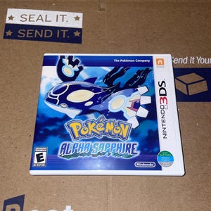 Può includere: Una cartuccia di gioco Nintendo 3DS per Pokemon Alpha Sapphire. Il gioco presenta un'immagine blu e bianca del Pokemon Kyogre sulla copertina.