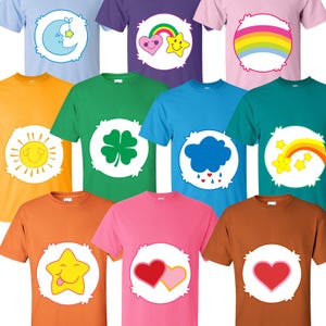 May include: A collection of nine short-sleeved t-shirts in various colours, each featuring a large white circular emblem on the chest. The emblems display colourful graphic icons including a moon, rainbow, sun, clover, cloud, and hearts.