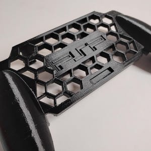 May include: Black plastic phone grip with a honeycomb design and the word "ELITE" printed on it.