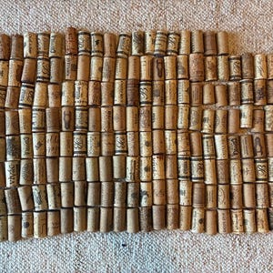 Puede incluir: Una disposición rectangular de numerosos tapones de corcho cilíndricos para vino, cada uno con logotipos, marcas y textos impresos únicos. Los corchos están colocados verticalmente en filas y columnas, creando un mosaico denso y texturizado.