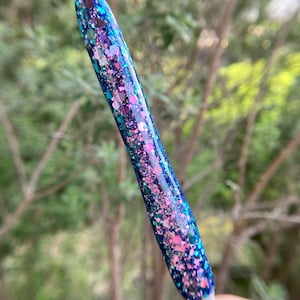 May include: A close-up of a blue, pink, and green glitter-filled crochet hook.