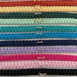 May include: A collection of macrame dog collars in various colors, including red, orange, yellow, green, teal, blue, navy, purple, pink, black, and white. Each collar features a metal ring for leash attachment.